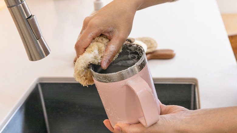Manos lavándose el vaso de metal rosa en el fregadero