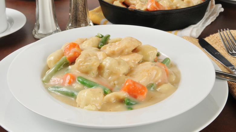 Un plato de pollo al estilo sureño y albóndigas en un recipiente blanco sobre un plato blanco.