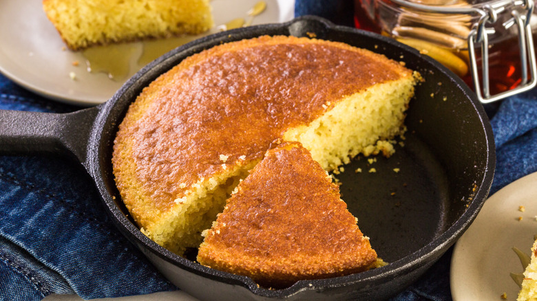 Sartén de hierro fundido con pan de maíz en rodajas sobre un mantel de mezclilla con platos variados alrededor.