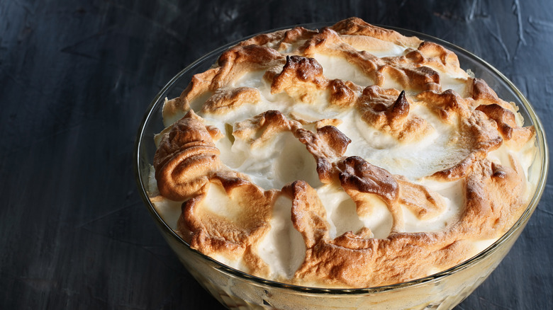 Un plato de pudín de plátano con merengue tostado en un recipiente de vidrio sobre un fondo de color oscuro
