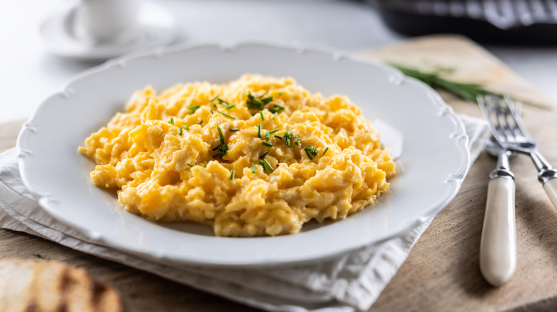 Un plato de huevos revueltos sobre un plato blanco sobre una mesa con una servilleta y cubiertos