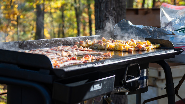 Tocino y patatas cocinando en una plancha al aire libre