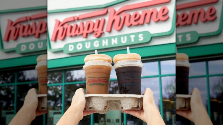 Bebidas Krispy Kreme para llevar con donas glaseadas encima sostenidas frente a un cartel de una tienda