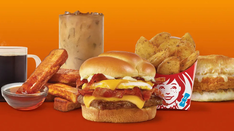 Variedad de elementos del menú de desayuno de Wendy's sobre un fondo naranja