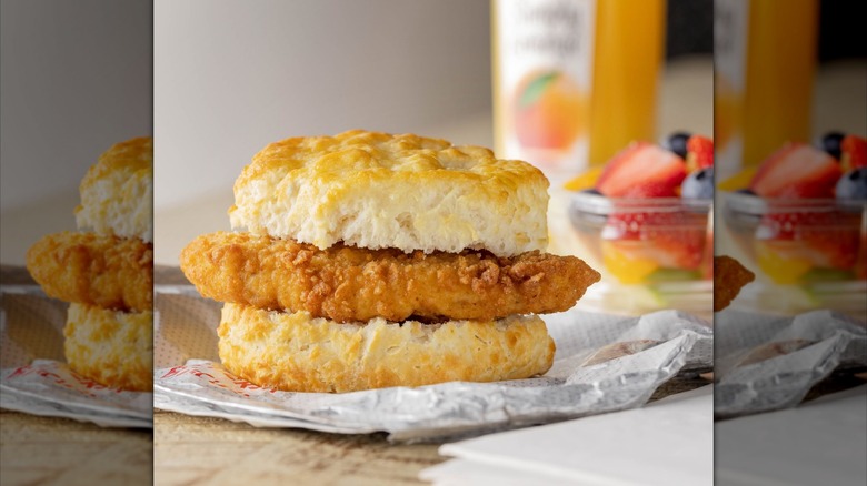 Una galleta de pollo Chick-fil-A con una taza de fruta borrosa y una botella de jugo de naranja Simply al fondo