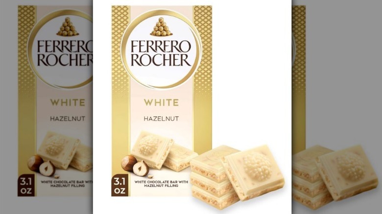 Barra de avellana blanca Ferrero Rocher en un paquete dorado con trozos de chocolate blanco delante sobre fondo blanco