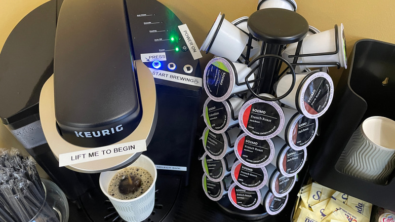 Cafetera Keurig negra preparando una taza y un soporte lleno de monodosis de café al lado.