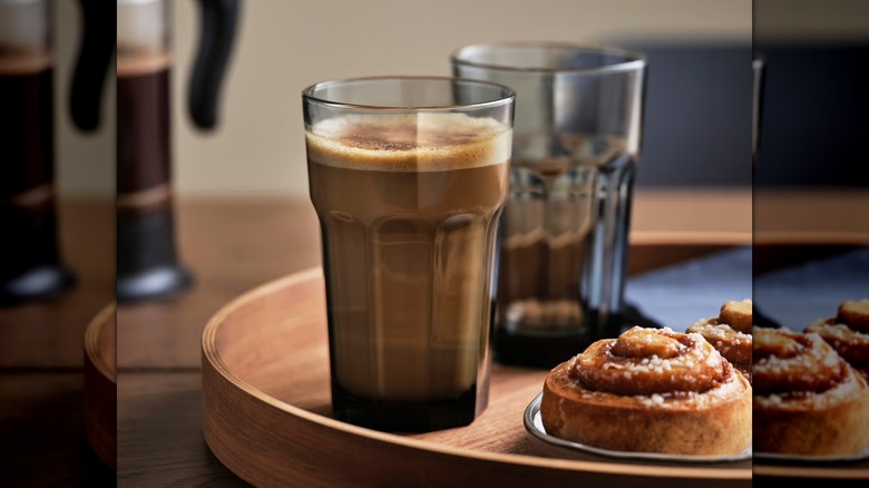 Café en una taza de cristal con un pastel en una bandeja