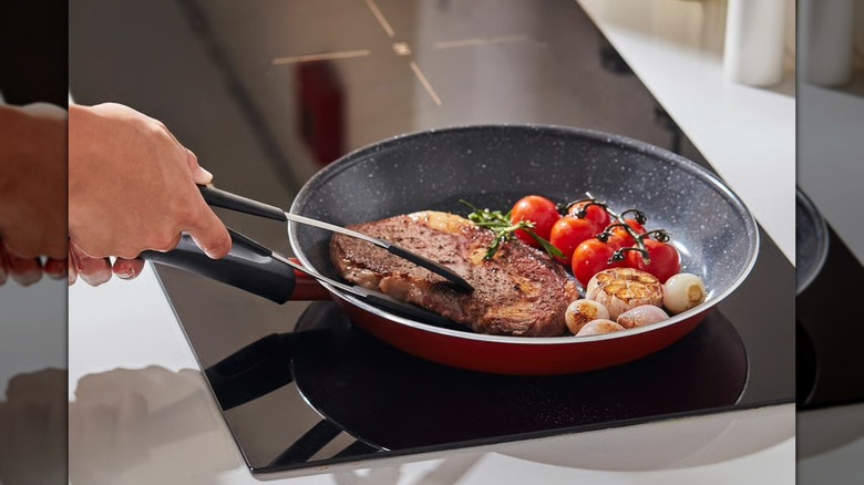 Sartén antiadherente roja y negra con bistec y verduras en la estufa