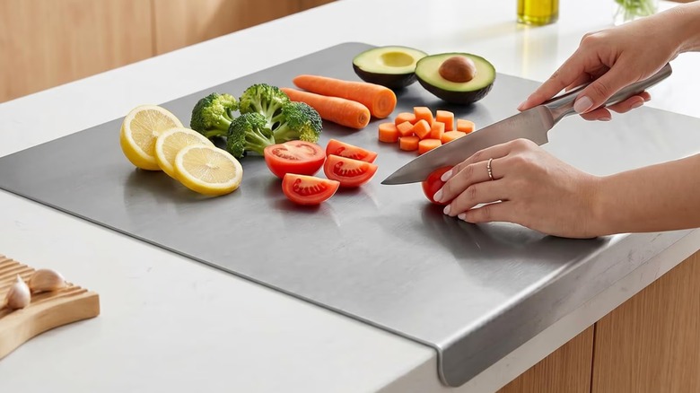 Una persona que sostiene un cuchillo para cortar verduras y frutas en una tabla de cortar de acero