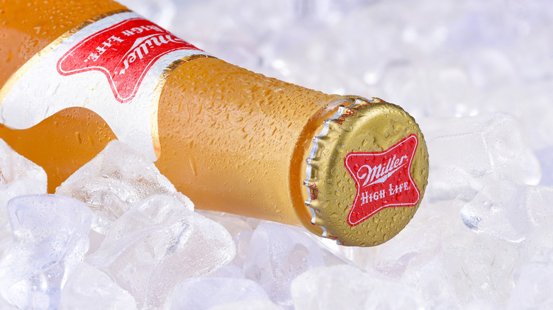 Botella de cerveza Miller High Life de lado en hielo, con la tapa mirando a la cámara