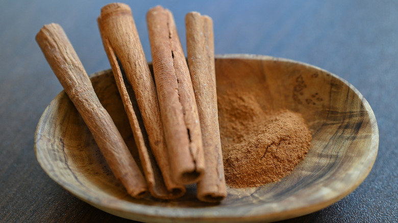 Un cuenco de madera con ramas de canela molidas y enteras.