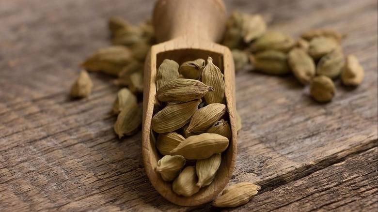 Una pala de madera con vainas de cardamomo sobre una mesa de madera