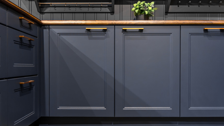 Gabinetes de cocina azul marino con herrajes dorados y encimeras de madera marrón.
