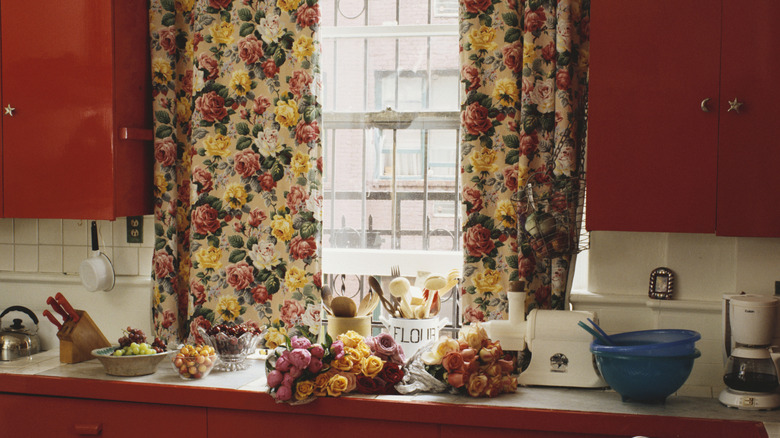 Una cocina vintage con gabinetes de color marrón rojizo y cortinas florales.