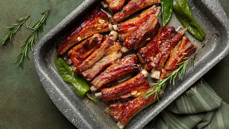 Bandeja de horno con costillas al horno rodeadas de pimientos y perejil