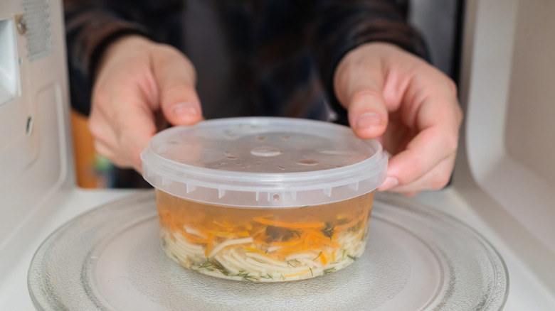 Manos colocando un recipiente de plástico con sopa en un microondas