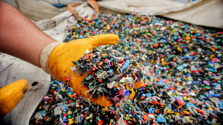Una mano enguantada metiendo la mano en un enorme contenedor de basura plástica.