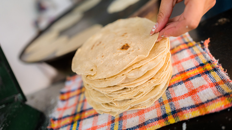 Sobre un paño de cocina sobre el mostrador hay una pila de tortillas de harina frescas.