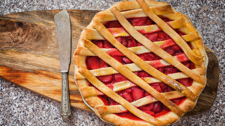 Tarta de fresas con una tapa de celosía sobre una tabla de madera junto a un cuchillo