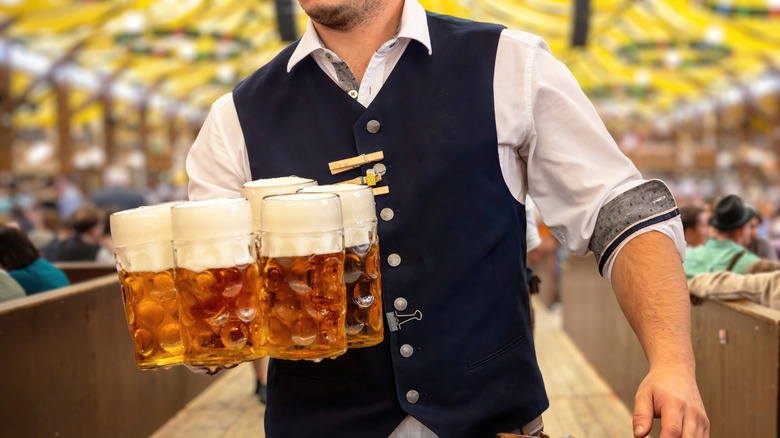 Cervecería de Munich con clientes a ambos lados de un camarero sosteniendo varias cervezas en grandes jarras de vidrio