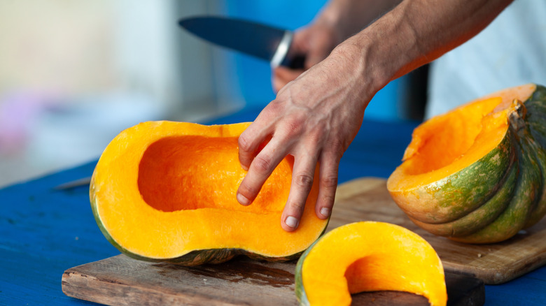 Una persona está cortando una calabaza en una tabla de cortar de madera.