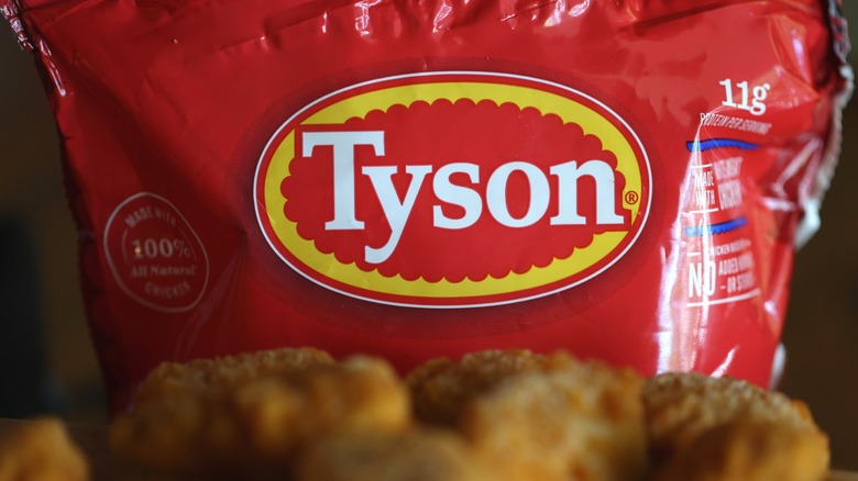 Un enfoque en la etiqueta de la marca Tyson en una bolsa roja detrás de nuggets de pollo borrosos