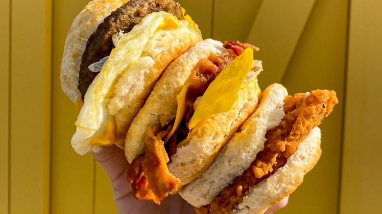 Mano sosteniendo tres sándwiches de desayuno Biscuitville