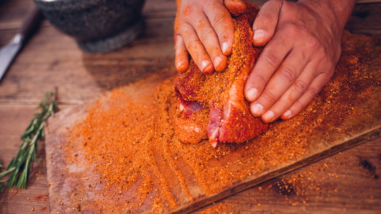 Las manos presionan un frote seco sobre un trozo de carne cruda sobre una tabla de cortar antes de cocinar