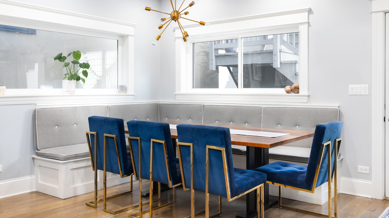 Banqueta inspirada en los años 60 en una cocina con sillas azul real y un banco de comedor gris.