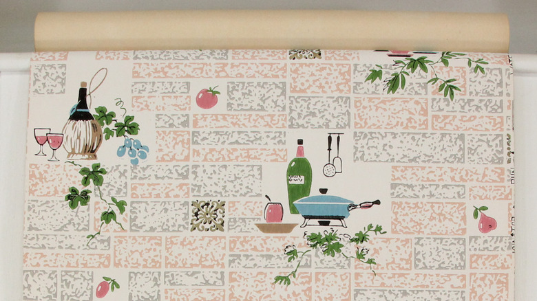 Un rollo de papel pintado estilo años 60 con botellas de vino, aceite, tomates, hojas y una sartén, entre otros elementos.