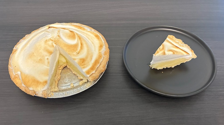 Frescura garantizada pastel de merengue de limón al que le falta una rodaja y una rodaja en un plato negro