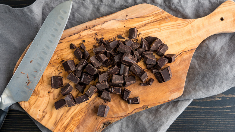Chocolate picado junto a un cuchillo sobre una tabla de cortar de madera rústica