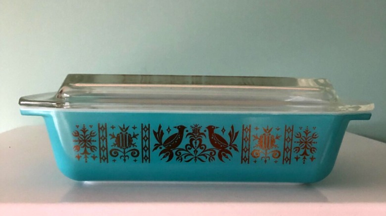 Cazuela de Pyrex con fondo turquesa y pájaros dorados y volutas en el frente