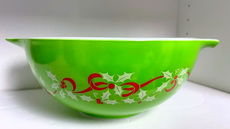 Un tazón de Pyrex festivo de color verde brillante con cinta roja y hojas de acebo blancas