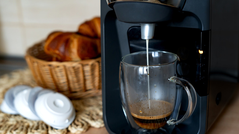 Cafetera preparando una taza de café junto a cápsulas de café y una cesta de pan