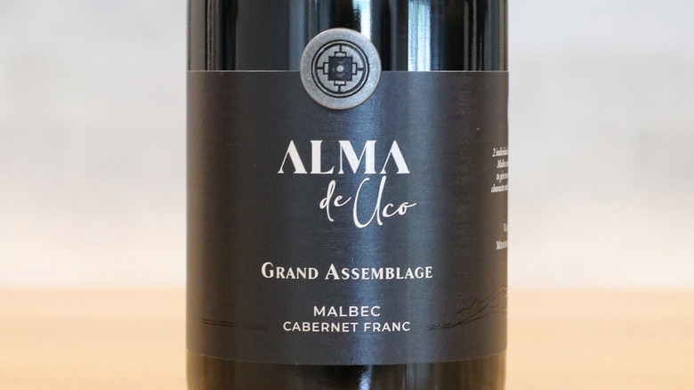 Botella de Alma de Uco Grand Assemblage y primer plano de la etiqueta negra sobre la mesa