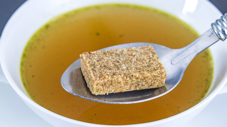 Cubo de caldo en una cuchara sobre sopa