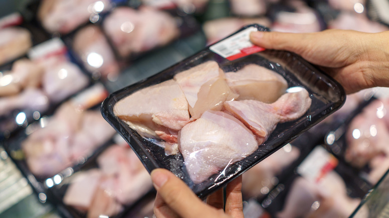 Una persona sosteniendo un paquete de pollo crudo en un supermercado.