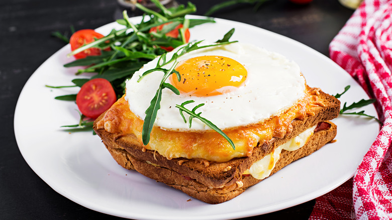 Un croque madame en un plato blanco con rúcula y tomates cherry