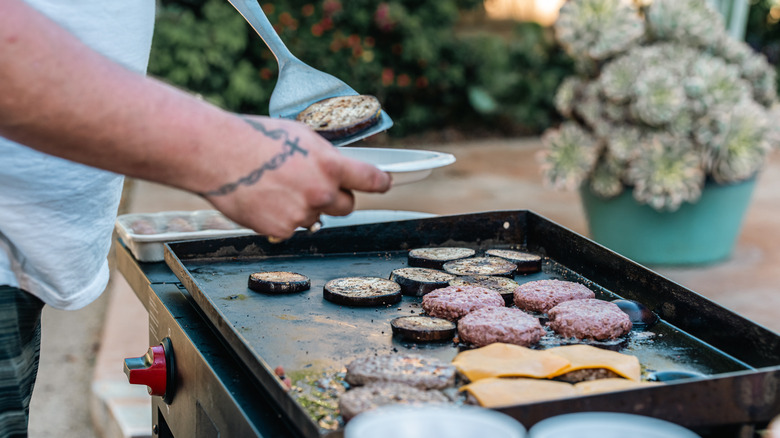 Hombre sirviéndose a sí mismo desde una parrilla plana llena de hamburguesas