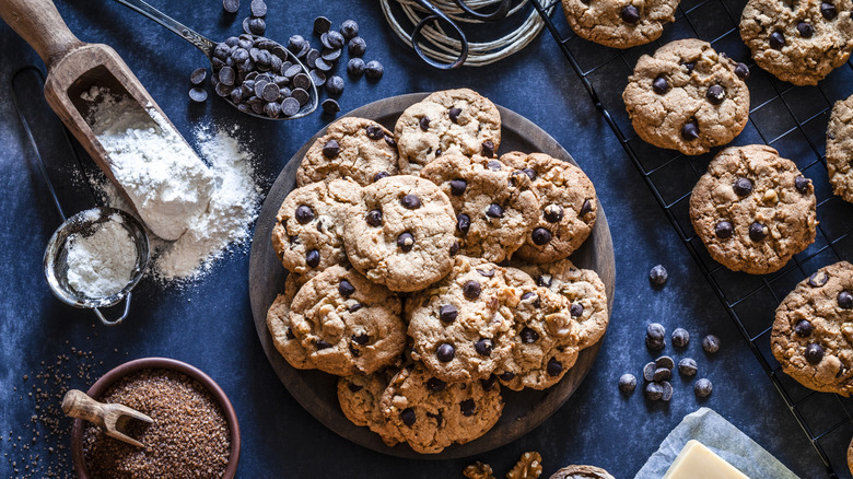 Plato de galletas con chispas de chocolate rodeado de ingredientes para hornear y rejilla para galletas