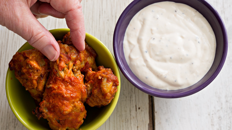 Una mano alcanza las alitas de pollo junto a la salsa de queso azul