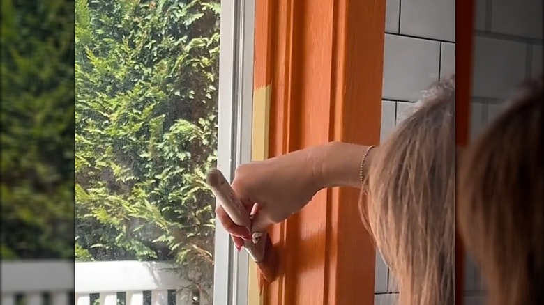 Mujer pintando el marco de la ventana con pintura naranja