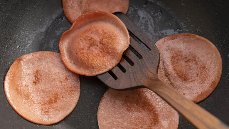 Bolonia frita en sartén con espátula de madera