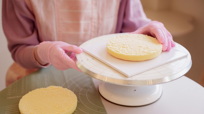 Baker colocando pastel de vainilla sobre un plato giratorio de pastel blanco