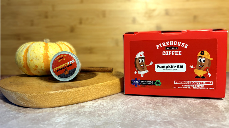 Una cápsula de Firehouse Coffee Pumpkin-itis apoyada contra una calabaza, al lado de la caja de donde proviene.