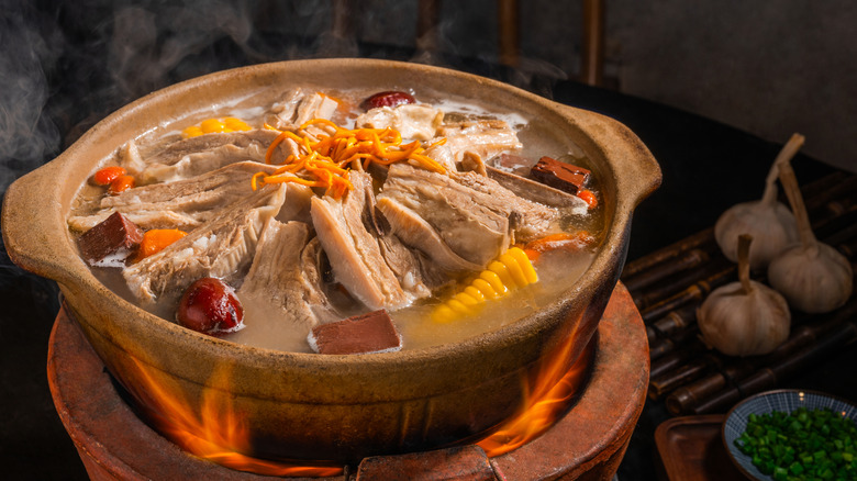 Una olla de sopa al estilo chino cocinada sobre un fuego vivo con alliums al fondo