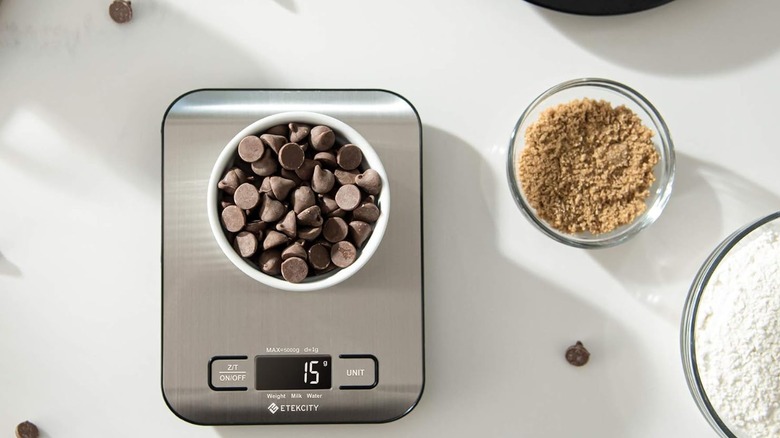 Balanza digital plateada con un cuenco de chispas de chocolate encima, junto a otros cuencos