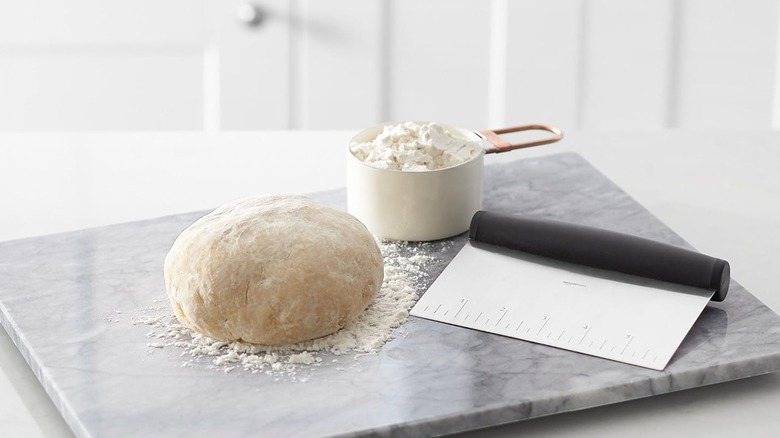 masa, raspador, taza de harina sobre tabla de mármol